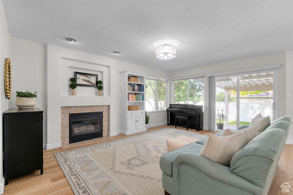 Living area with a tile fireplace, light wood-style floors, baseboards, and a textured ceiling