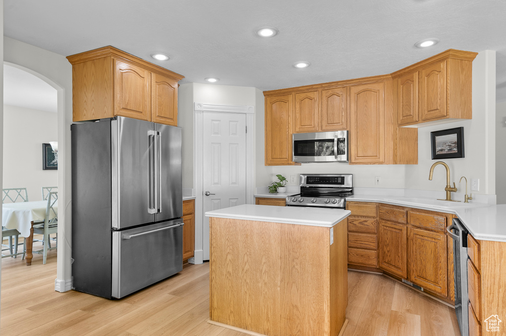 Kitchen with appliances with stainless steel finishes, a sink, light wood-style floors, a kitchen island, and arched walkways