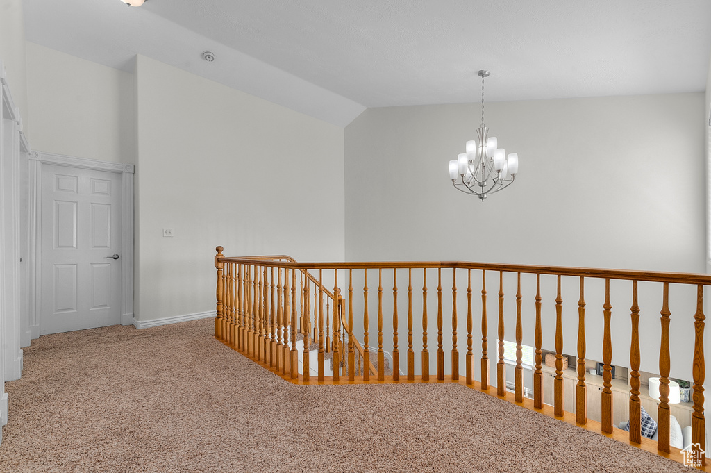 Corridor featuring carpet, a chandelier, vaulted ceiling, an upstairs landing, and baseboards