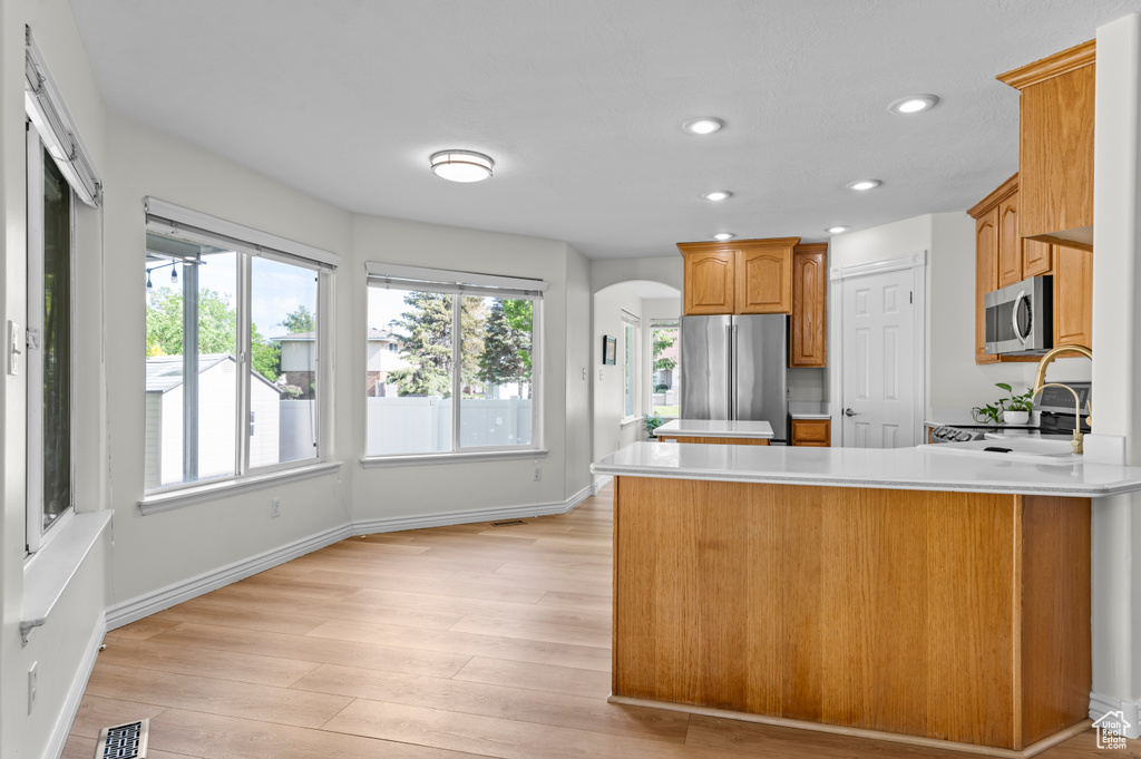 Kitchen with appliances with stainless steel finishes, a peninsula, light countertops, light wood-style floors, and arched walkways