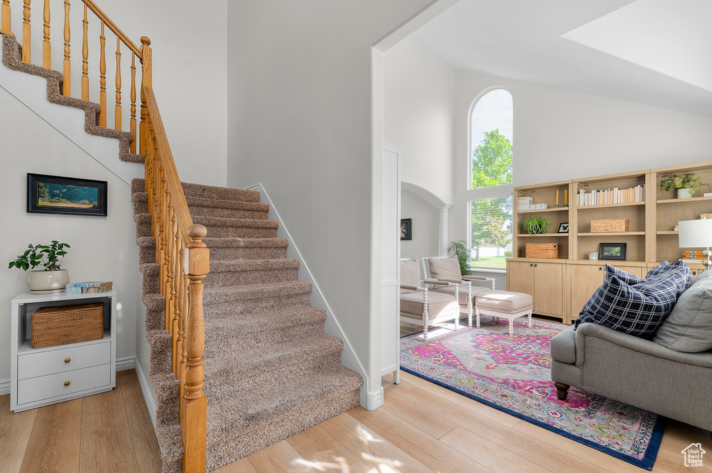 Staircase featuring wood finished floors, high vaulted ceiling, arched walkways, and baseboards
