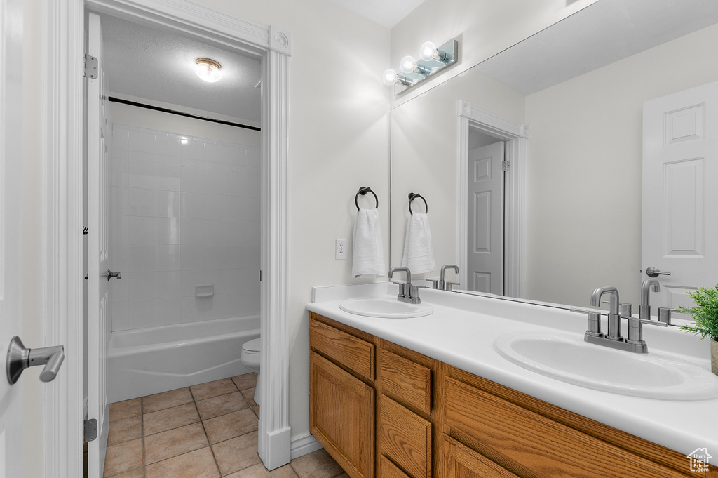 Bathroom with toilet, double vanity, tile patterned flooring, and shower / washtub combination