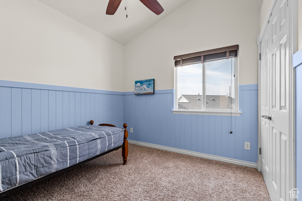 Bedroom featuring lofted ceiling, a wainscoted wall, carpet flooring, a closet, and ceiling fan
