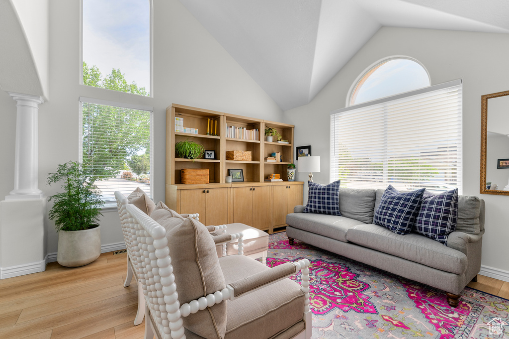 Living room with decorative columns, light wood-style floors, high vaulted ceiling, and baseboards