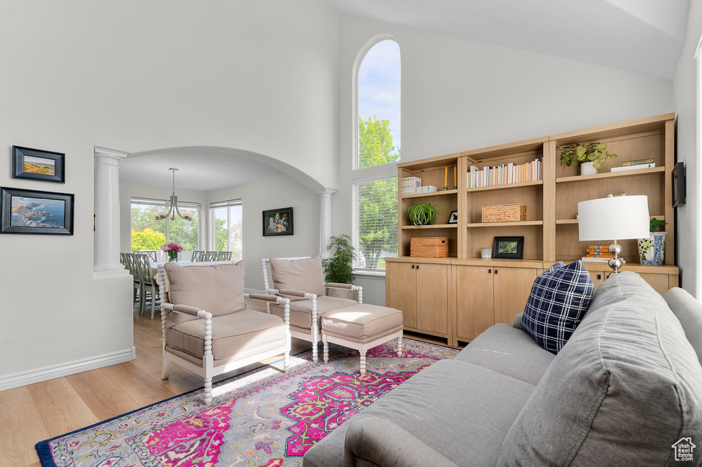 Living area with ornate columns, light wood-style flooring, high vaulted ceiling, arched walkways, and baseboards