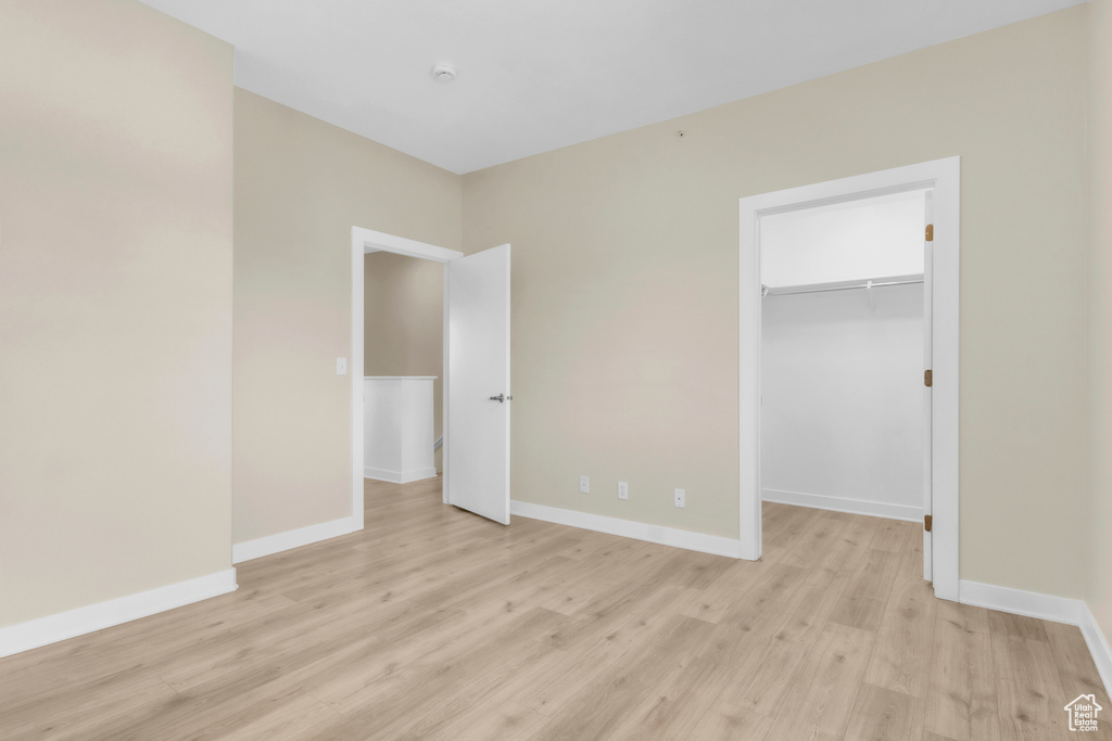 Unfurnished bedroom with light wood finished floors, a spacious closet, baseboards, and a closet