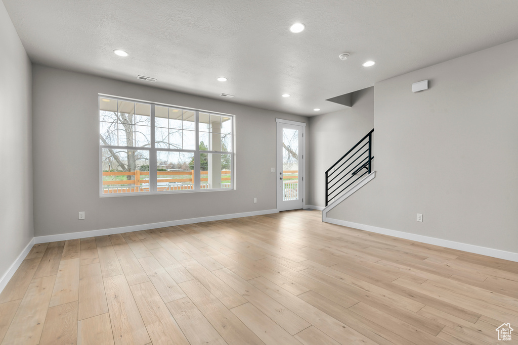 Unfurnished living room featuring stairs, recessed lighting, baseboards, and light wood-type flooring