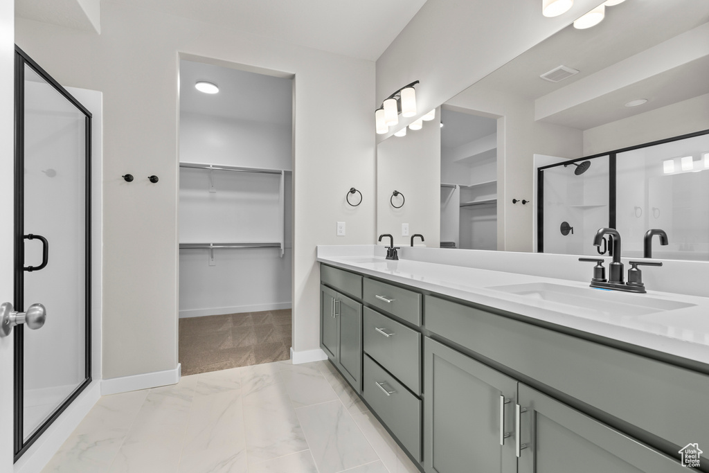 Bathroom with a walk in closet, a stall shower, double vanity, and baseboards