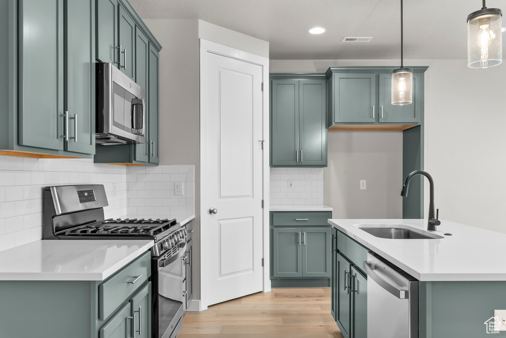 Kitchen featuring stainless steel appliances, a sink, light wood-style floors, pendant lighting, and light countertops