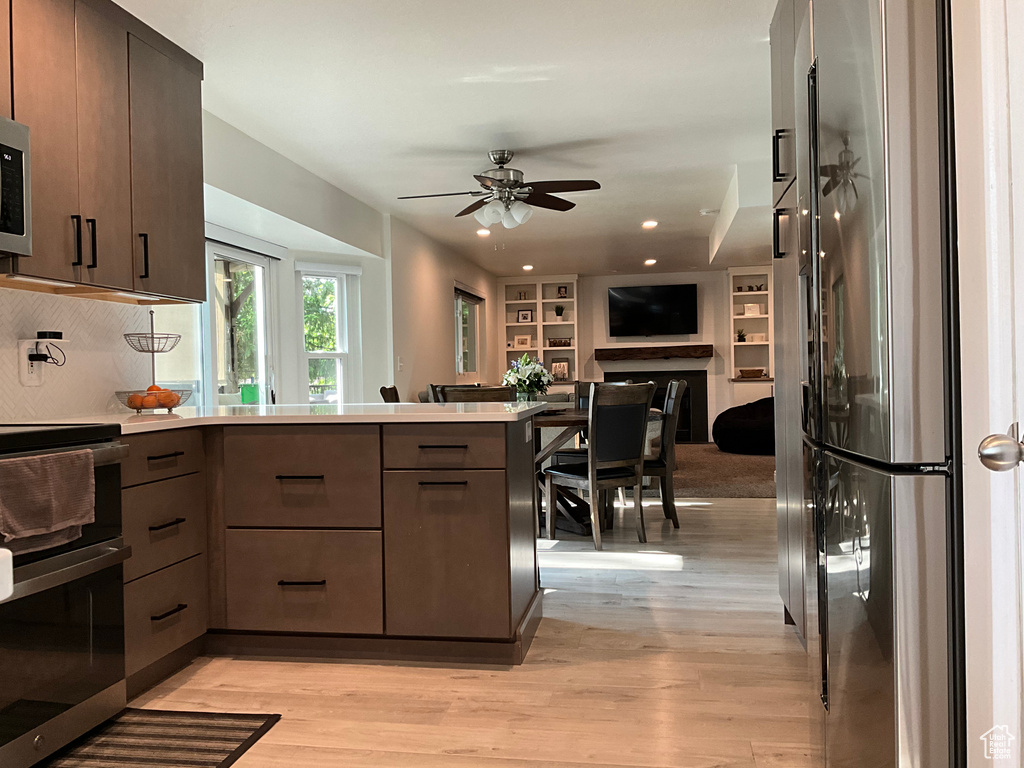 Kitchen with appliances with stainless steel finishes, a peninsula, open floor plan, light wood-style floors, and recessed lighting