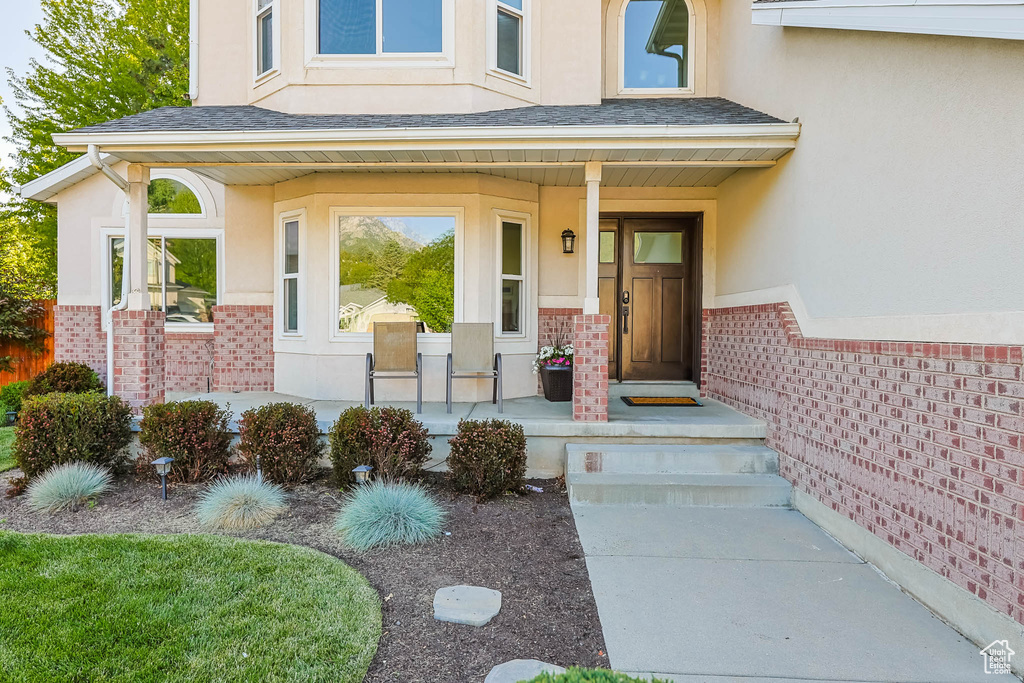 View of exterior entry featuring a porch, brick siding, stucco siding, and roof with shingles