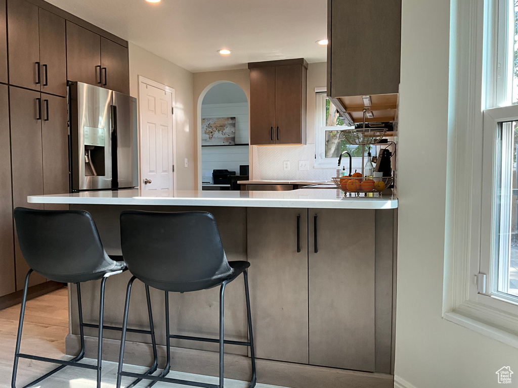 Kitchen featuring stainless steel fridge with ice dispenser, a peninsula, a kitchen breakfast bar, backsplash, and light countertops