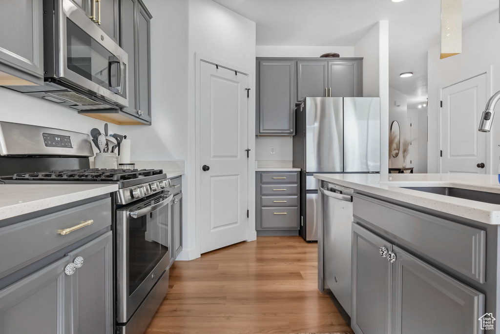 Kitchen featuring stainless steel appliances, gray cabinetry, a sink, light wood finished floors, and light stone counters