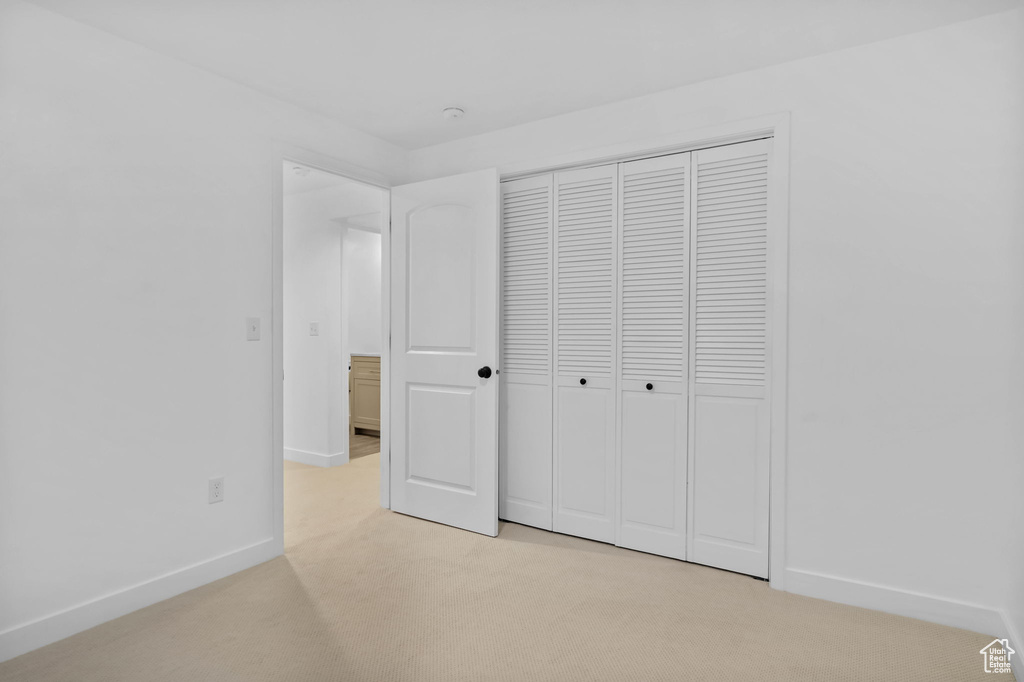 Unfurnished bedroom with light colored carpet, baseboards, and a closet