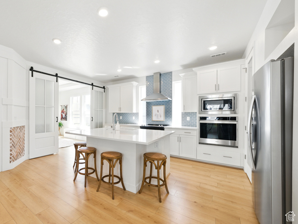 Kitchen featuring stainless steel appliances, wall chimney exhaust hood, a breakfast bar, light countertops, and white cabinets
