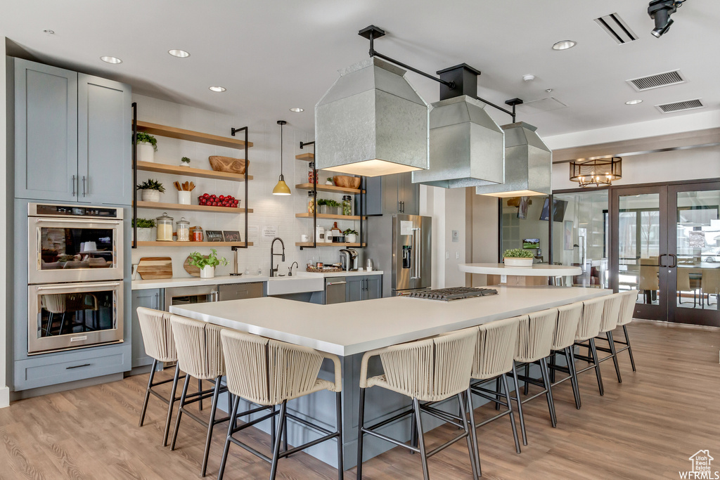 Kitchen with a sink, open shelves, light countertops, stainless steel appliances, and a breakfast bar area