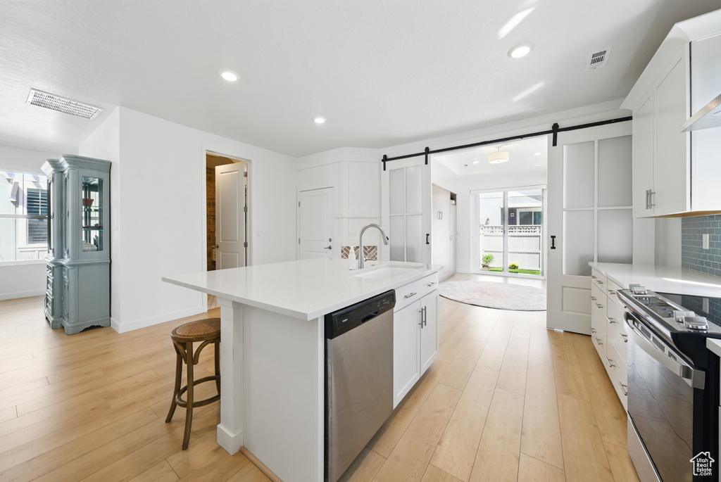 Kitchen with appliances with stainless steel finishes, a sink, a barn door, light wood-style floors, and white cabinetry