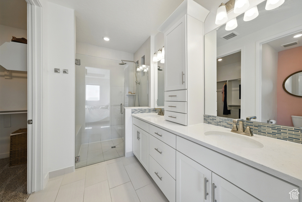 Bathroom with a stall shower, a walk in closet, double vanity, tile patterned flooring, and toilet