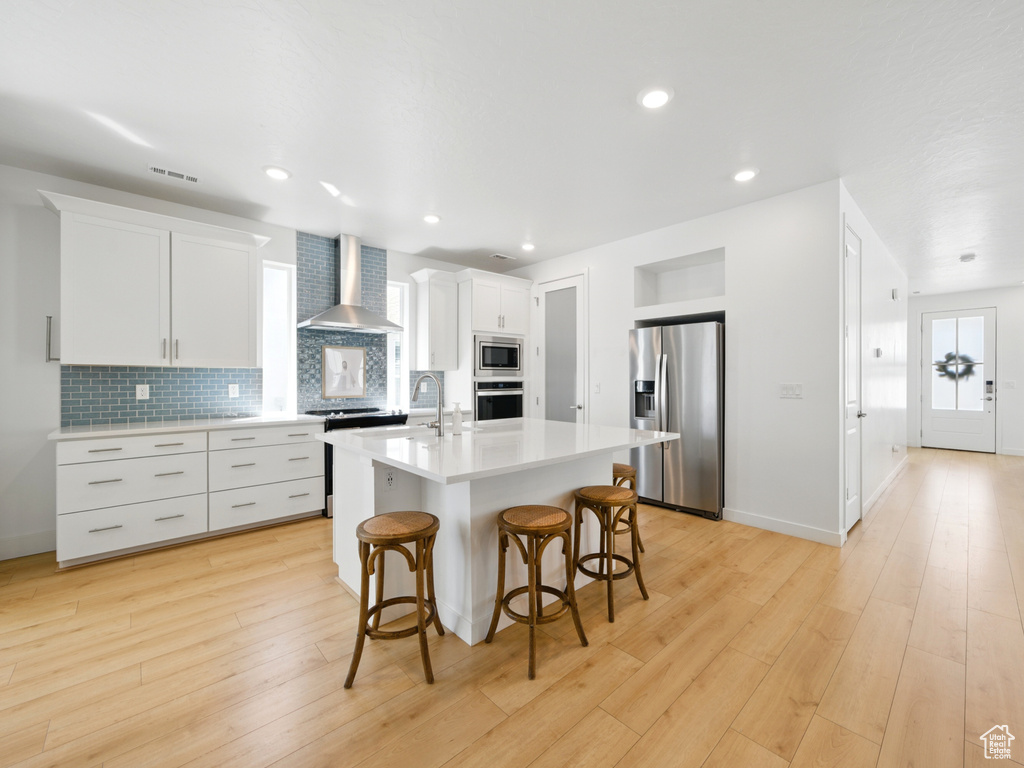 Kitchen featuring appliances with stainless steel finishes, wall chimney range hood, light countertops, a breakfast bar area, and decorative backsplash