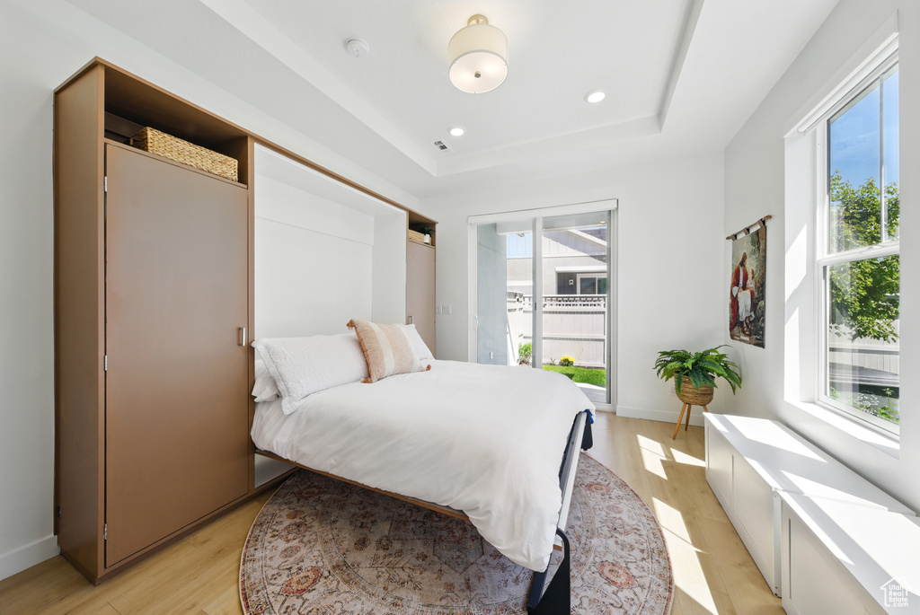 Bedroom featuring multiple windows, a tray ceiling, light wood finished floors, recessed lighting, and baseboards
