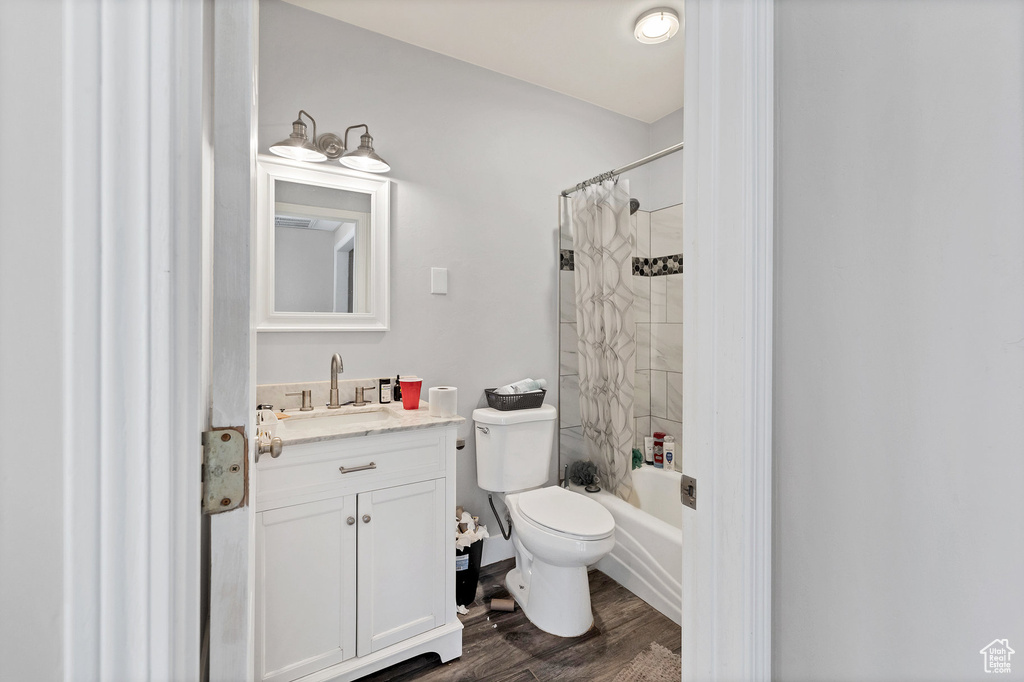 Full bathroom with vanity, toilet, wood finished floors, and shower / bath combination with curtain