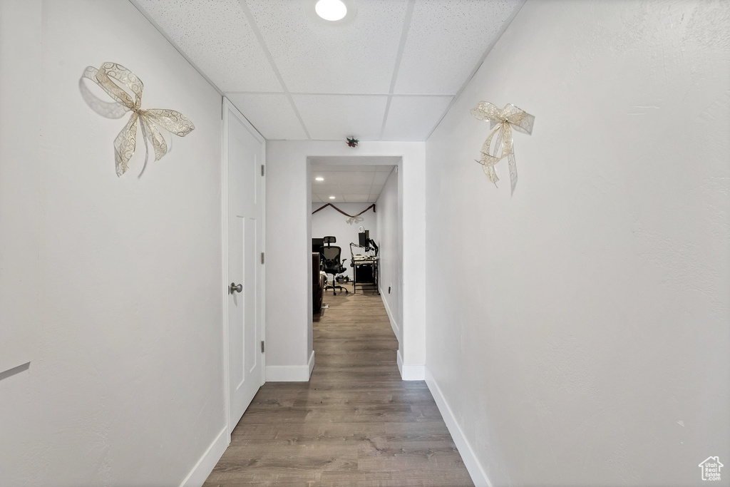 Corridor with light wood-style floors, a paneled ceiling, baseboards, and a desk