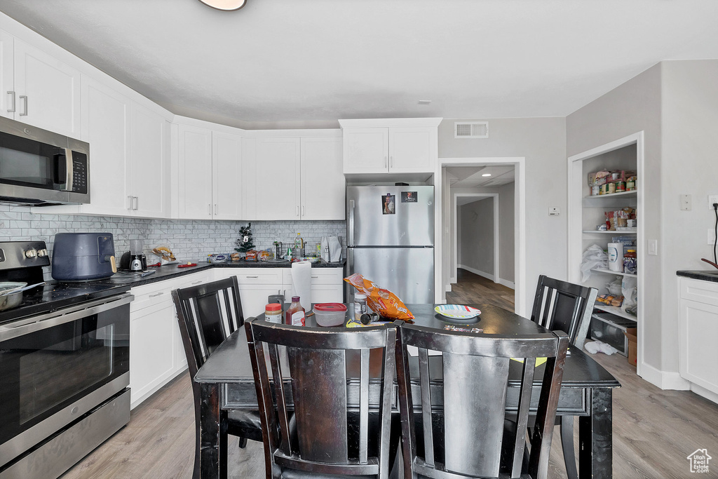 Kitchen with stainless steel appliances, dark countertops, tasteful backsplash, and light wood-style floors