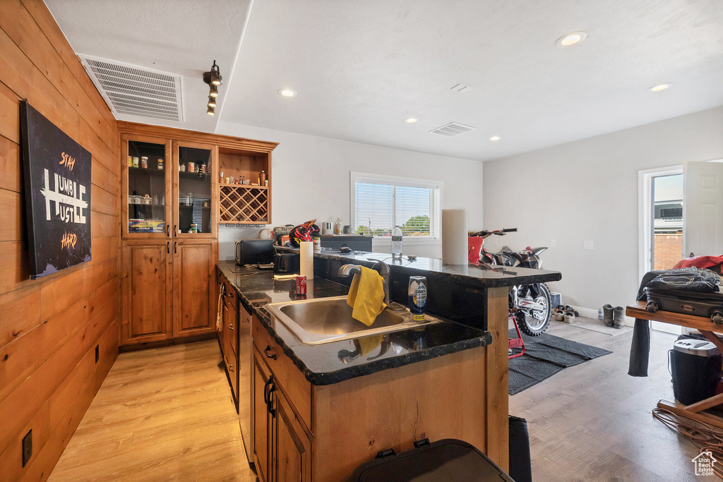 Kitchen featuring light wood finished floors, a sink, brown cabinetry, recessed lighting, and glass insert cabinets