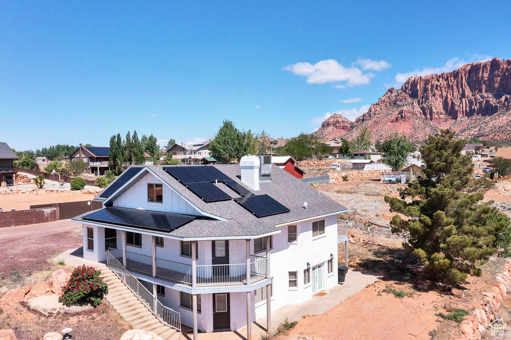 Rear view of house with a balcony, roof mounted solar panels, roof with shingles, a chimney, and covered porch
