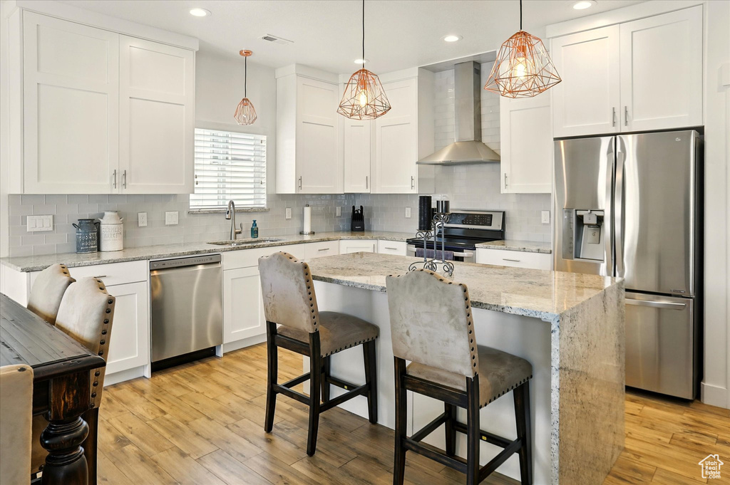 Kitchen featuring appliances with stainless steel finishes, wall chimney range hood, a sink, white cabinetry, and recessed lighting