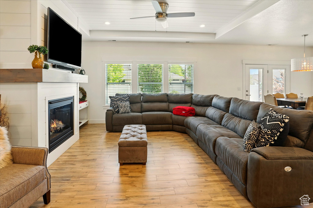 Living area with ceiling fan, a raised ceiling, light wood-type flooring, a glass covered fireplace, and recessed lighting