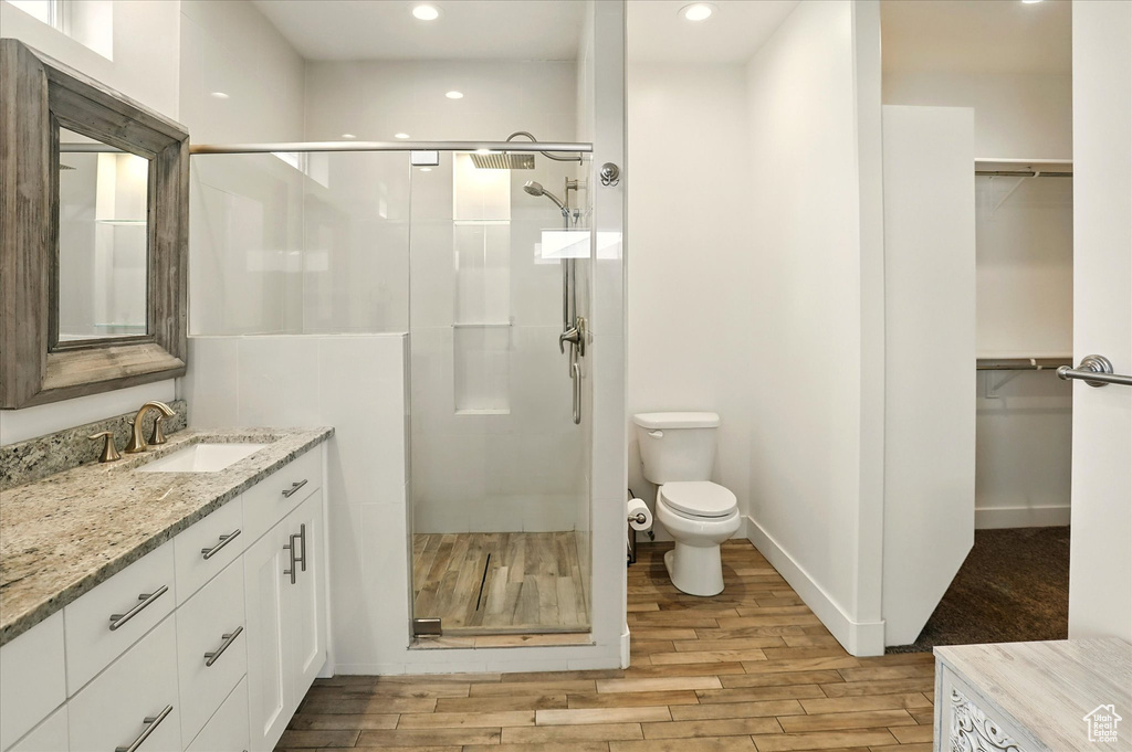 Bathroom featuring a stall shower, toilet, vanity, wood finished floors, and recessed lighting