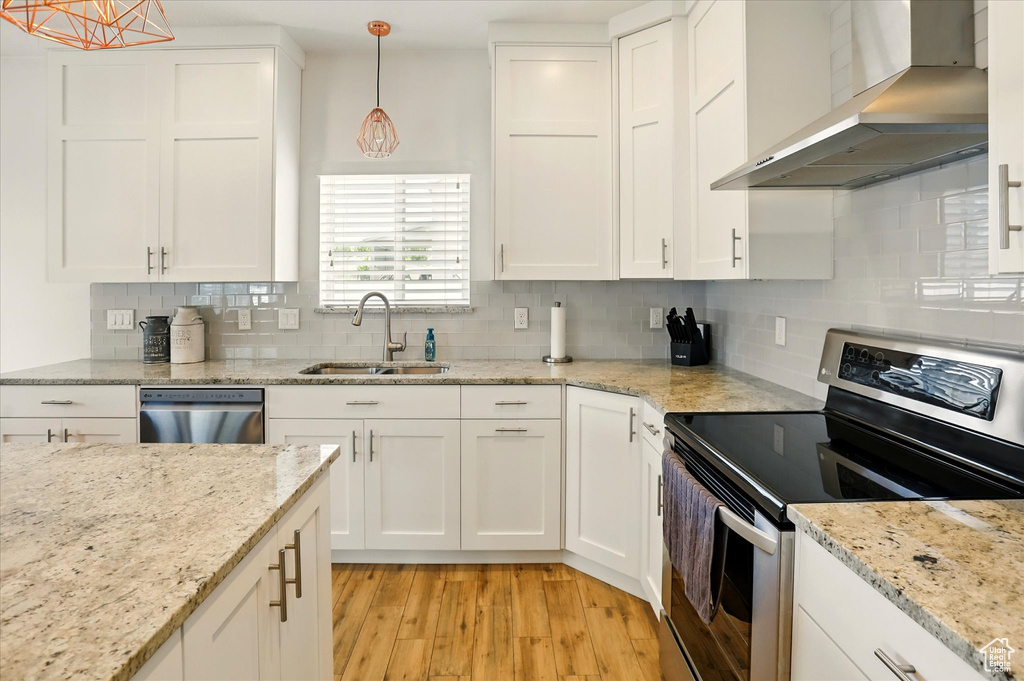 Kitchen with stainless steel appliances, wall chimney range hood, a sink, light wood-style floors, and white cabinetry