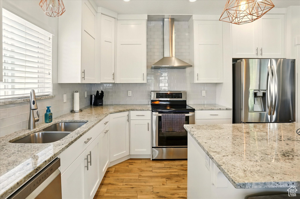 Kitchen with appliances with stainless steel finishes, wall chimney range hood, a sink, and white cabinets