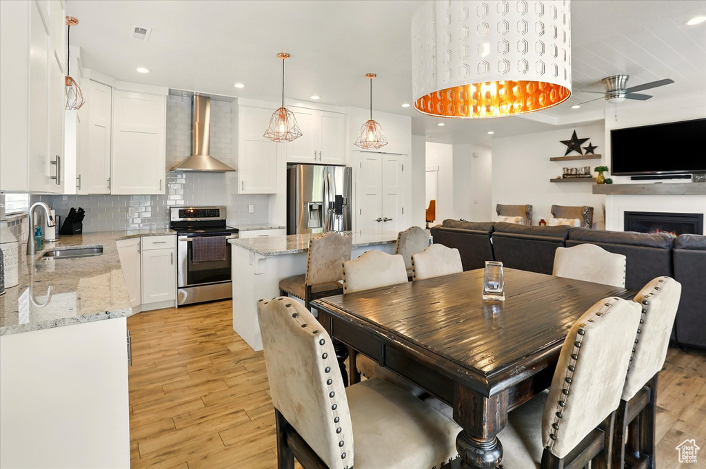 Dining space with light wood-style flooring, a ceiling fan, recessed lighting, and a warm lit fireplace