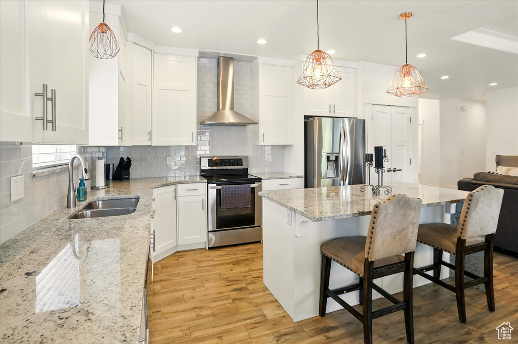 Kitchen with appliances with stainless steel finishes, wall chimney exhaust hood, a sink, light wood finished floors, and white cabinets