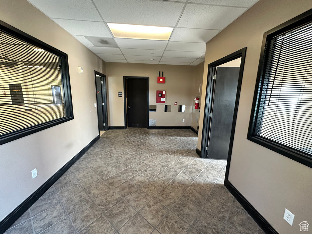 Hall with a drop ceiling, plenty of natural light, baseboards, and tile patterned floors
