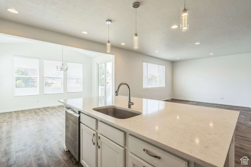 Kitchen featuring dishwasher, open floor plan, a center island with sink, dark wood finished floors, and a textured ceiling