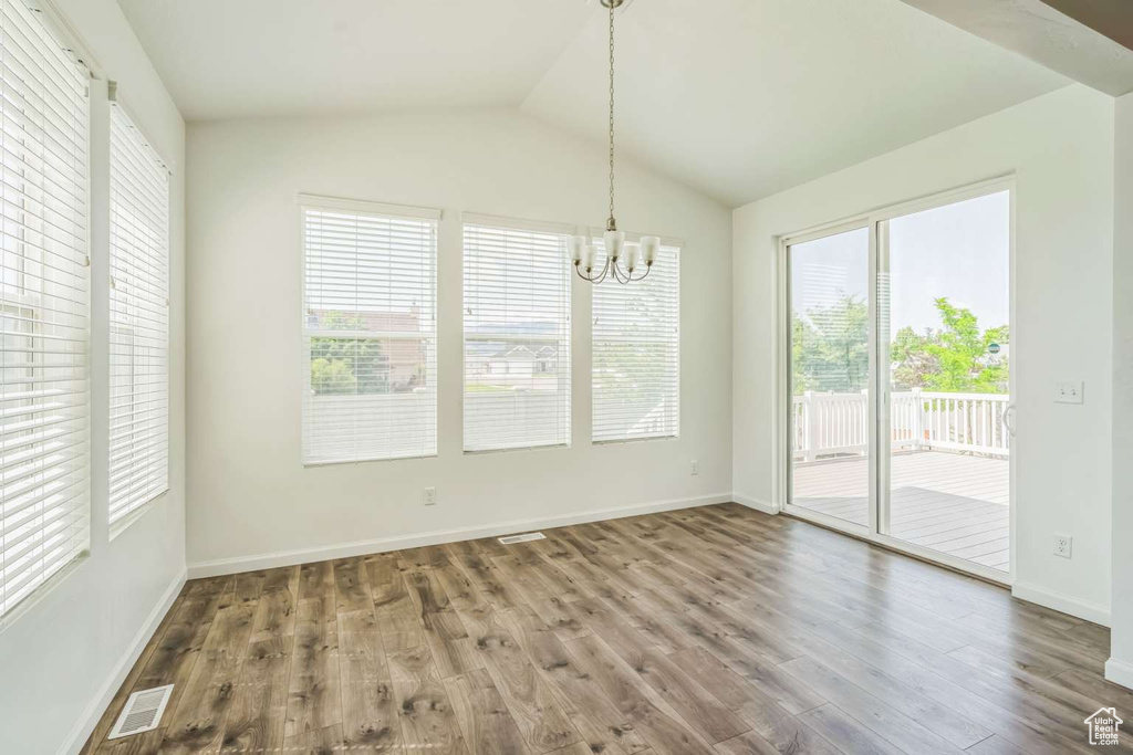Unfurnished dining area with a chandelier, wood finished floors, and vaulted ceiling