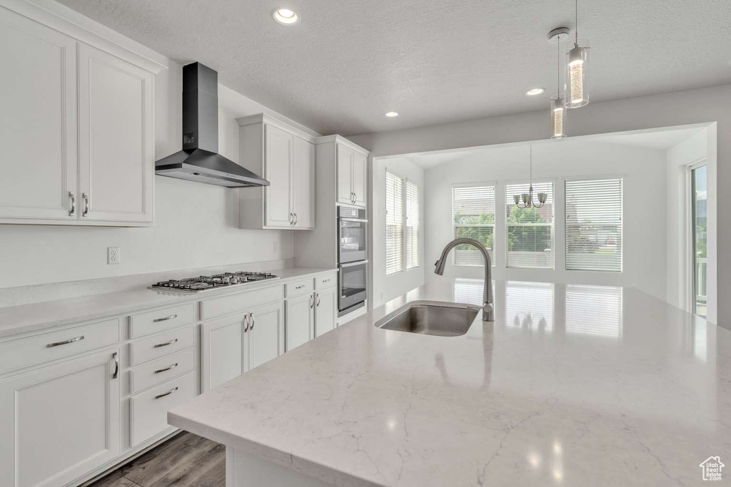 Kitchen featuring wall chimney exhaust hood, appliances with stainless steel finishes, a textured ceiling, recessed lighting, and white cabinetry