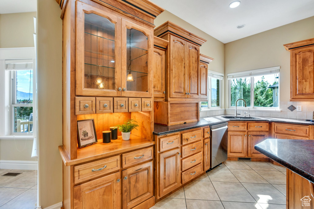 Kitchen featuring stainless steel dishwasher, a sink, tasteful backsplash, light tile patterned flooring, and plenty of natural light
