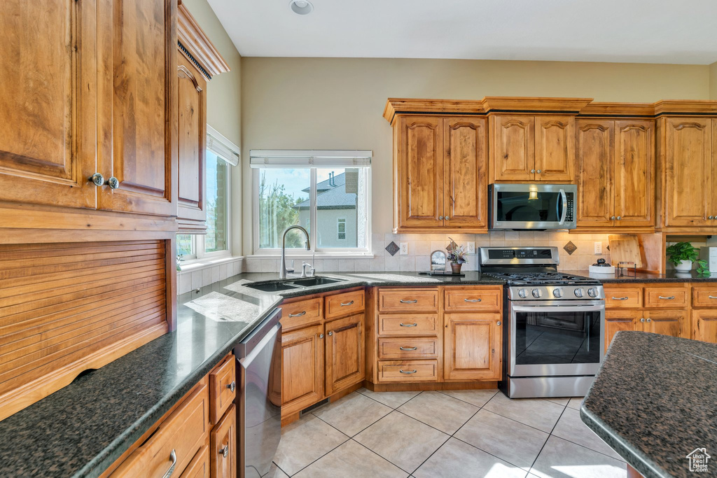Kitchen featuring stainless steel appliances, a sink, decorative backsplash, dark stone counters, and light tile patterned floors