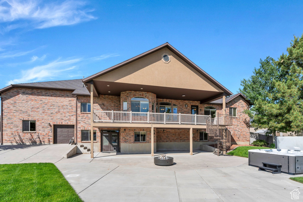 Back of house with a hot tub, a patio, brick siding, stairway, and a fire pit