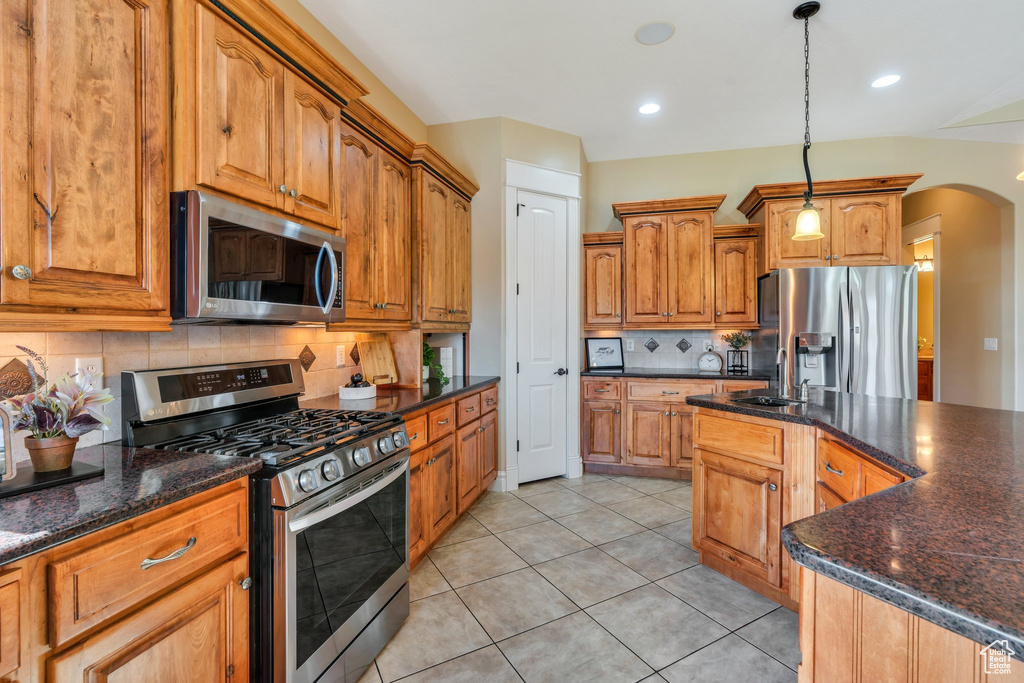 Kitchen with appliances with stainless steel finishes, a sink, tasteful backsplash, arched walkways, and light tile patterned floors