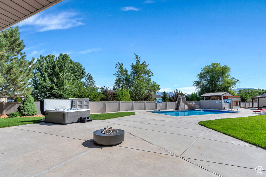 View of swimming pool featuring a water slide, an outdoor fire pit, and a patio area