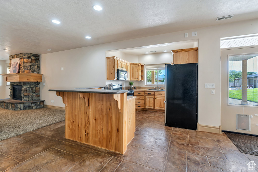 Kitchen with freestanding refrigerator, stainless steel electric range oven, black microwave, a breakfast bar, and a stone fireplace