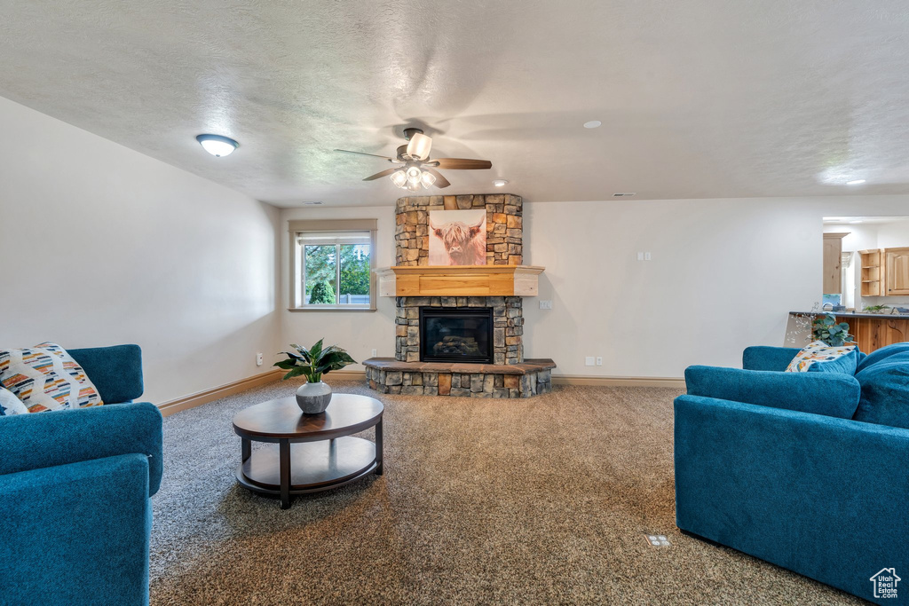Living area featuring ceiling fan, a fireplace, baseboards, carpet, and a textured ceiling