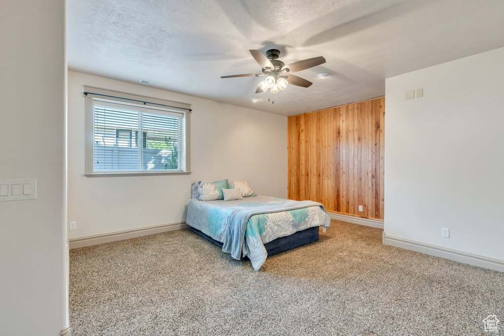 Carpeted bedroom with wood walls, baseboards, and a ceiling fan