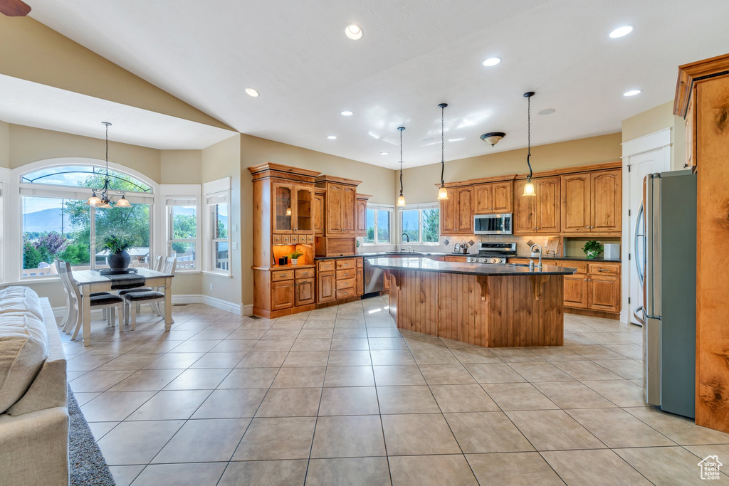 Kitchen featuring stainless steel appliances, a kitchen island, brown cabinets, open floor plan, and recessed lighting