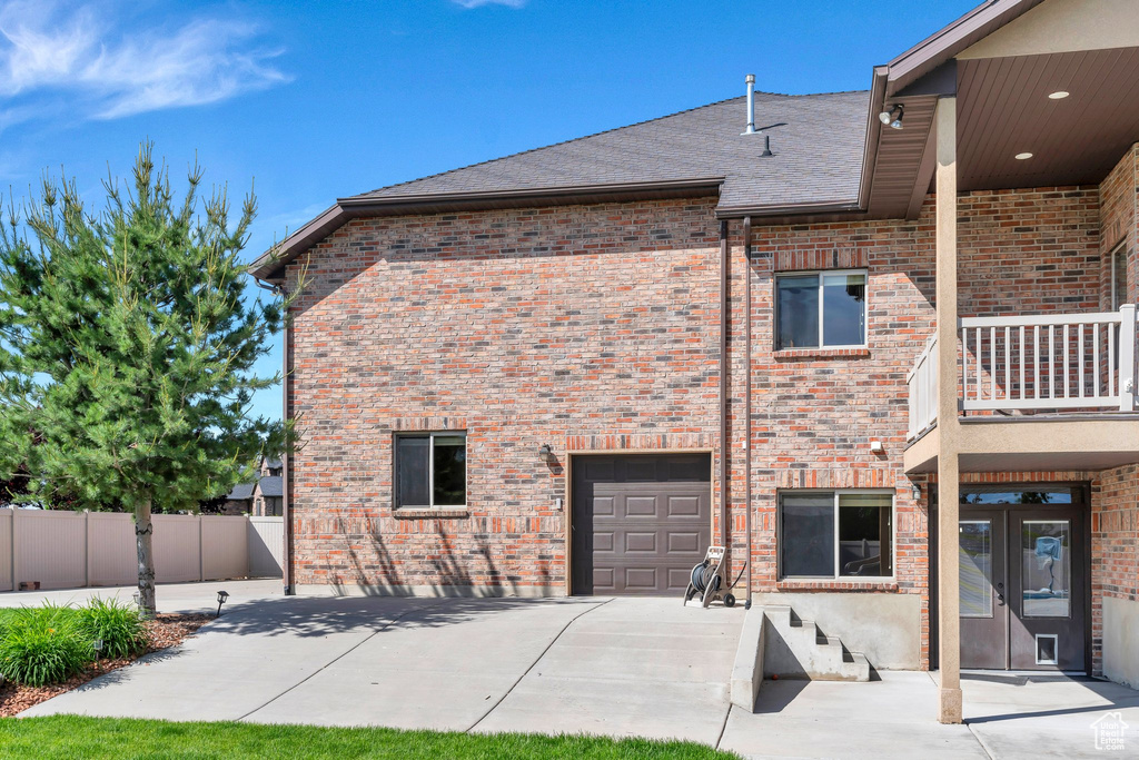Back of property with brick siding, a shingled roof, a balcony, concrete driveway, and french doors